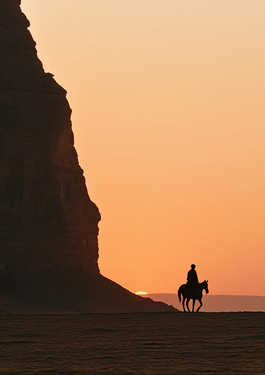 A lone rider at the cliff’s foot as the sun sets
