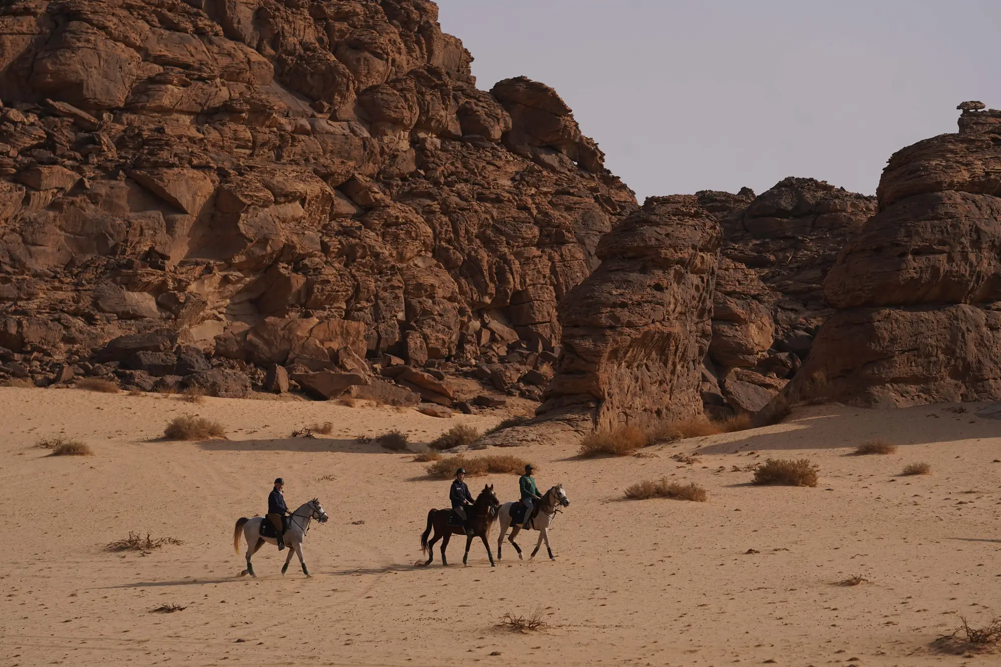 Riders small beneath the cliffs, crossing the land